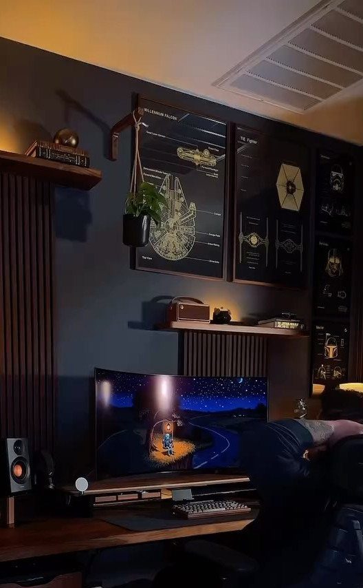 Dark gaming setup with wide monitor, black wall art, and wooden desk accents.
