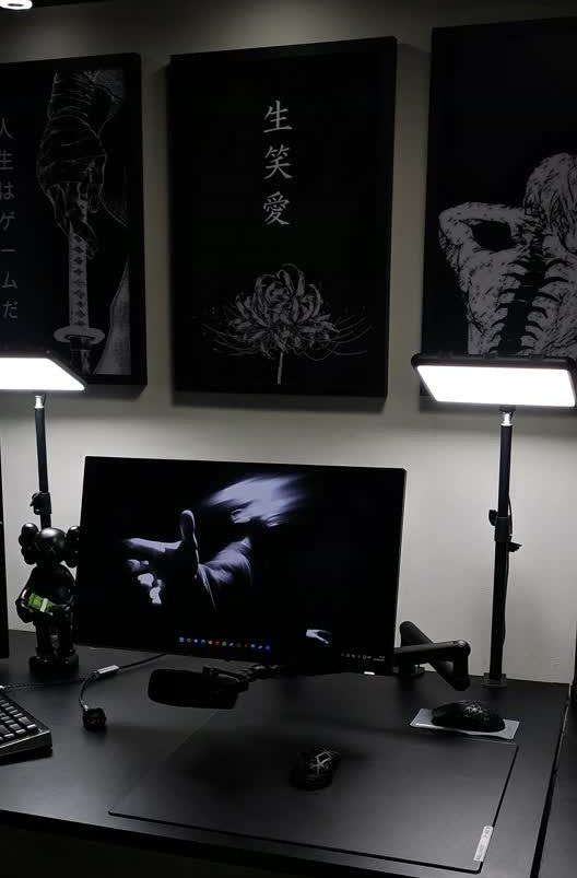 Black gaming setup with a monitor, desk lamps, and dark wall art prints.