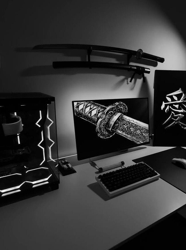 Black gaming desk with a PC, monitor, keyboard, and katanas on the wall.