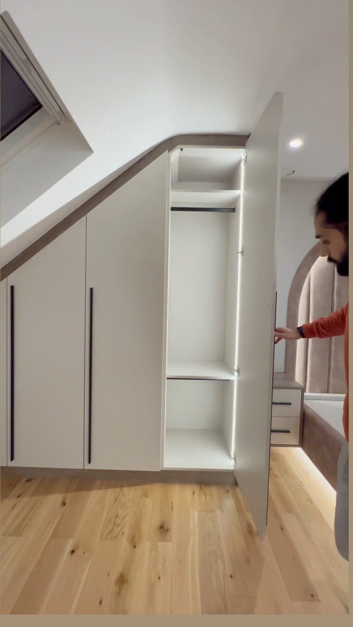 White built-in wardrobe under a sloped attic ceiling with light wood floors.