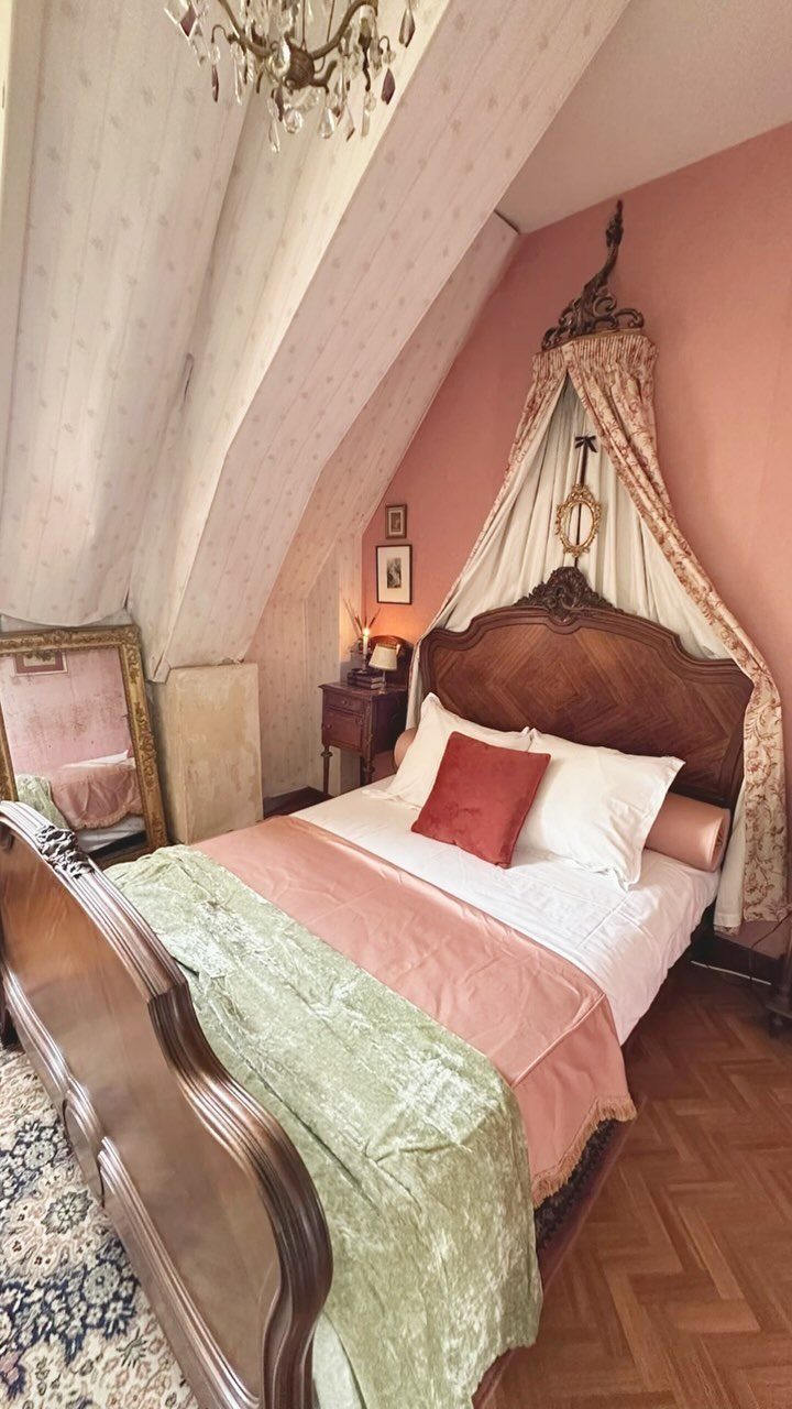 Attic bedroom with sloped ceilings, a canopy bed, and a crystal chandelier.