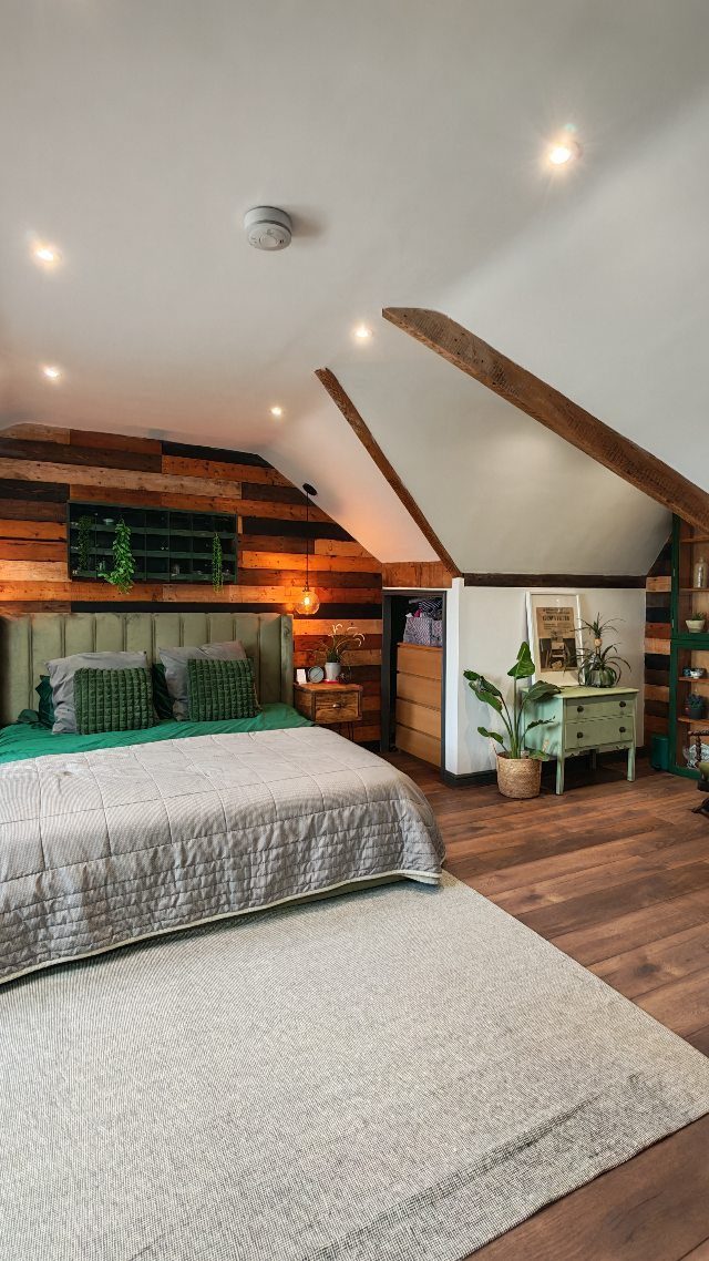 Attic bedroom with sloped ceilings, exposed wooden beams, and a rustic wood accent wall.