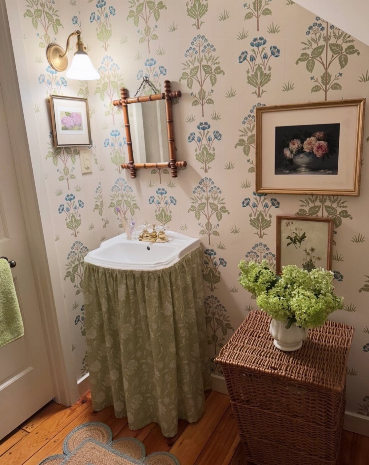 Small half bath with floral wallpaper, a skirted sink, and a wicker chest.