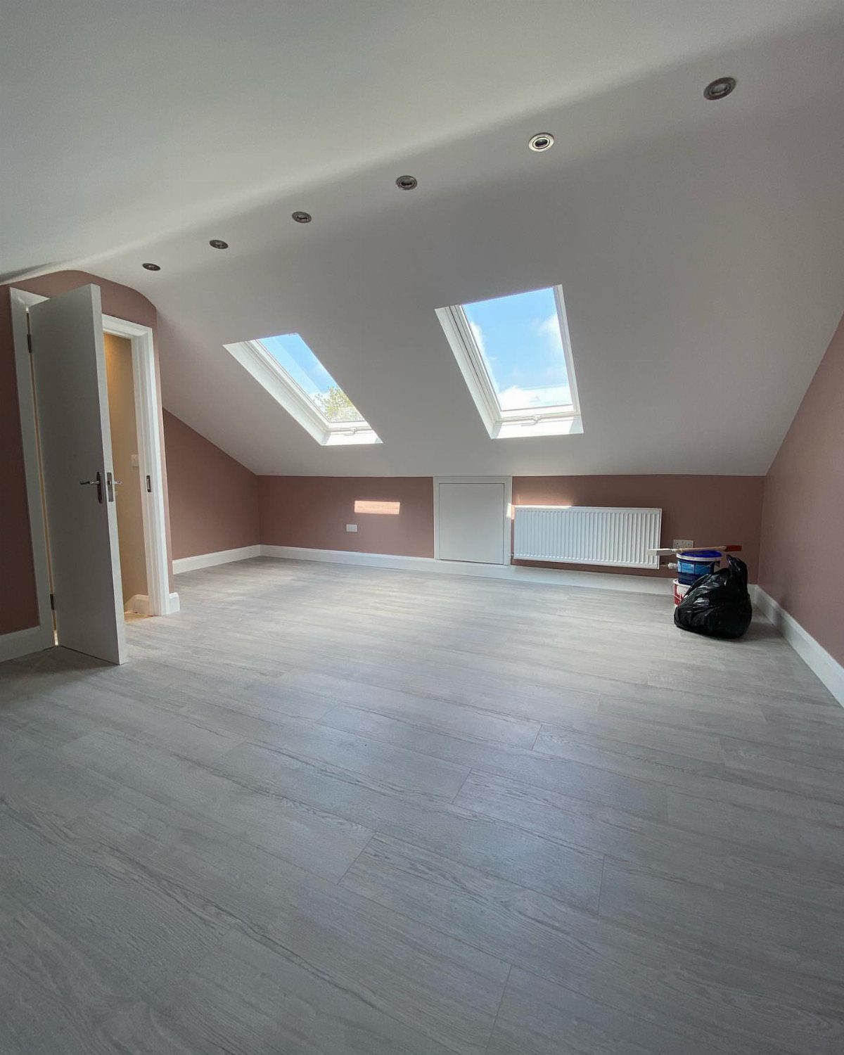 Empty attic bedroom with sloped ceilings, skylights, and light grey wood flooring.