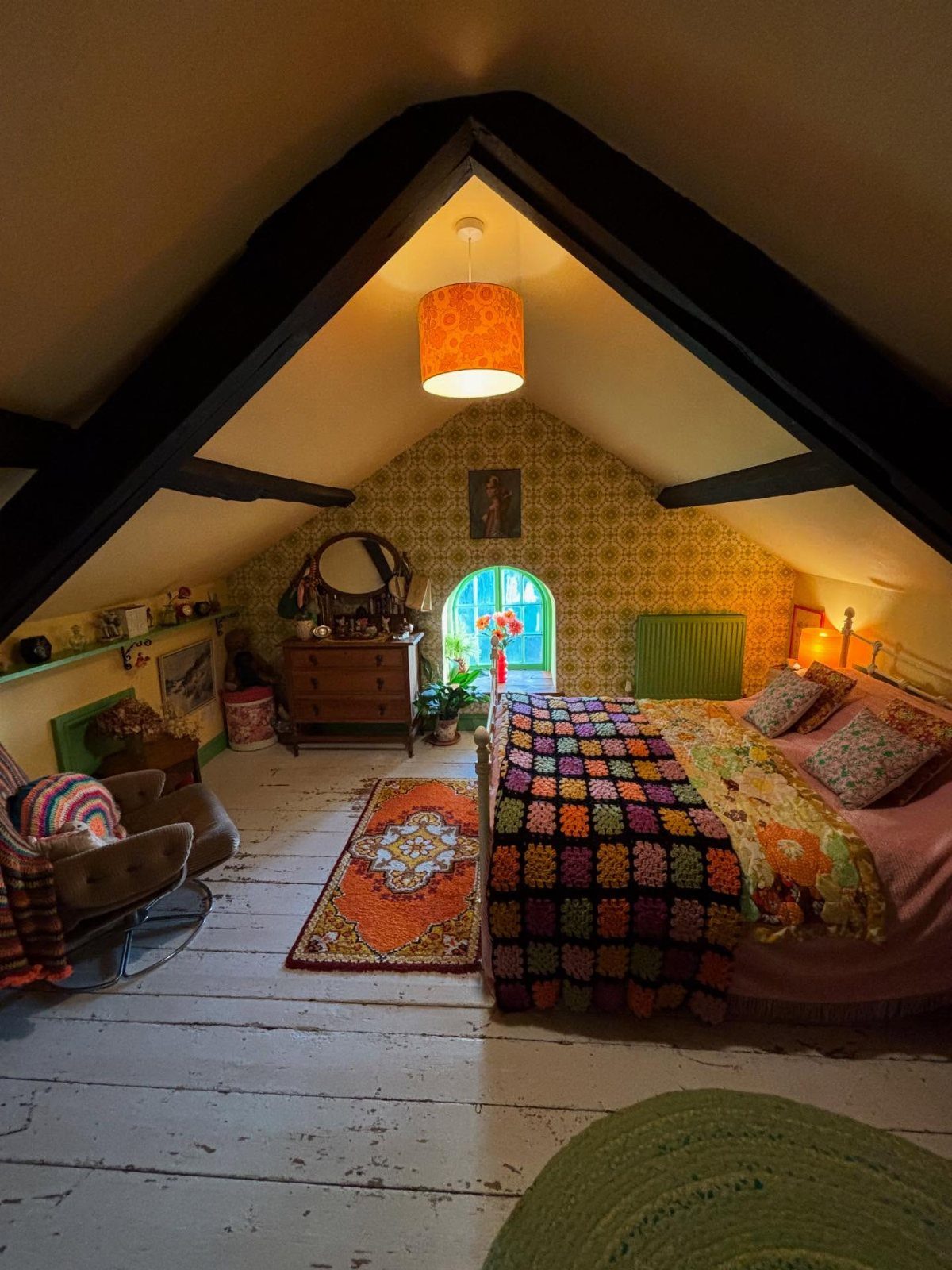 Attic bedroom with sloped ceilings, dark beams, and a colorful crochet bedspread.