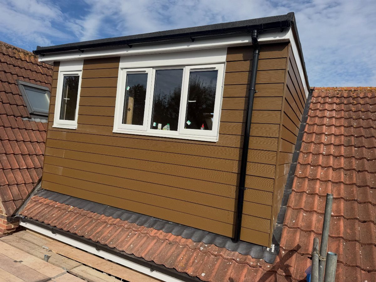 Brown wooden dormer extension with white windows on a red tiled roof.