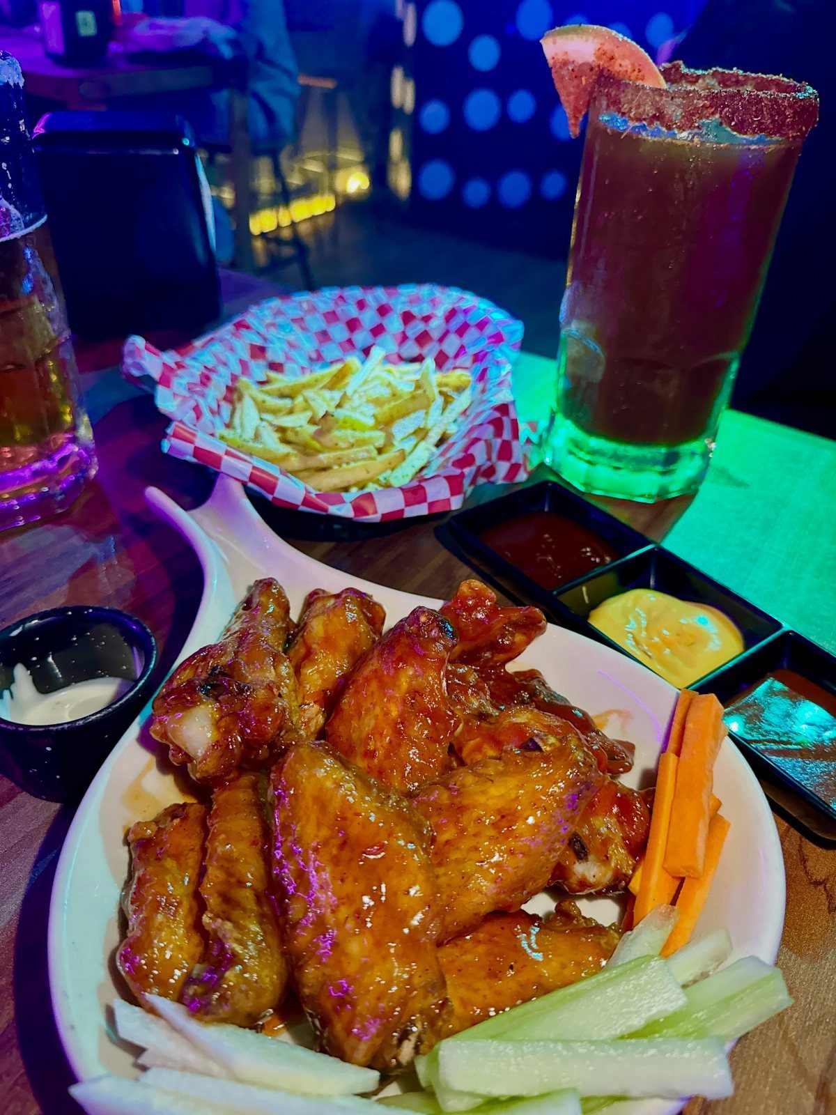 Glazed chicken wings, french fries, and a tall cocktail on a bar table.