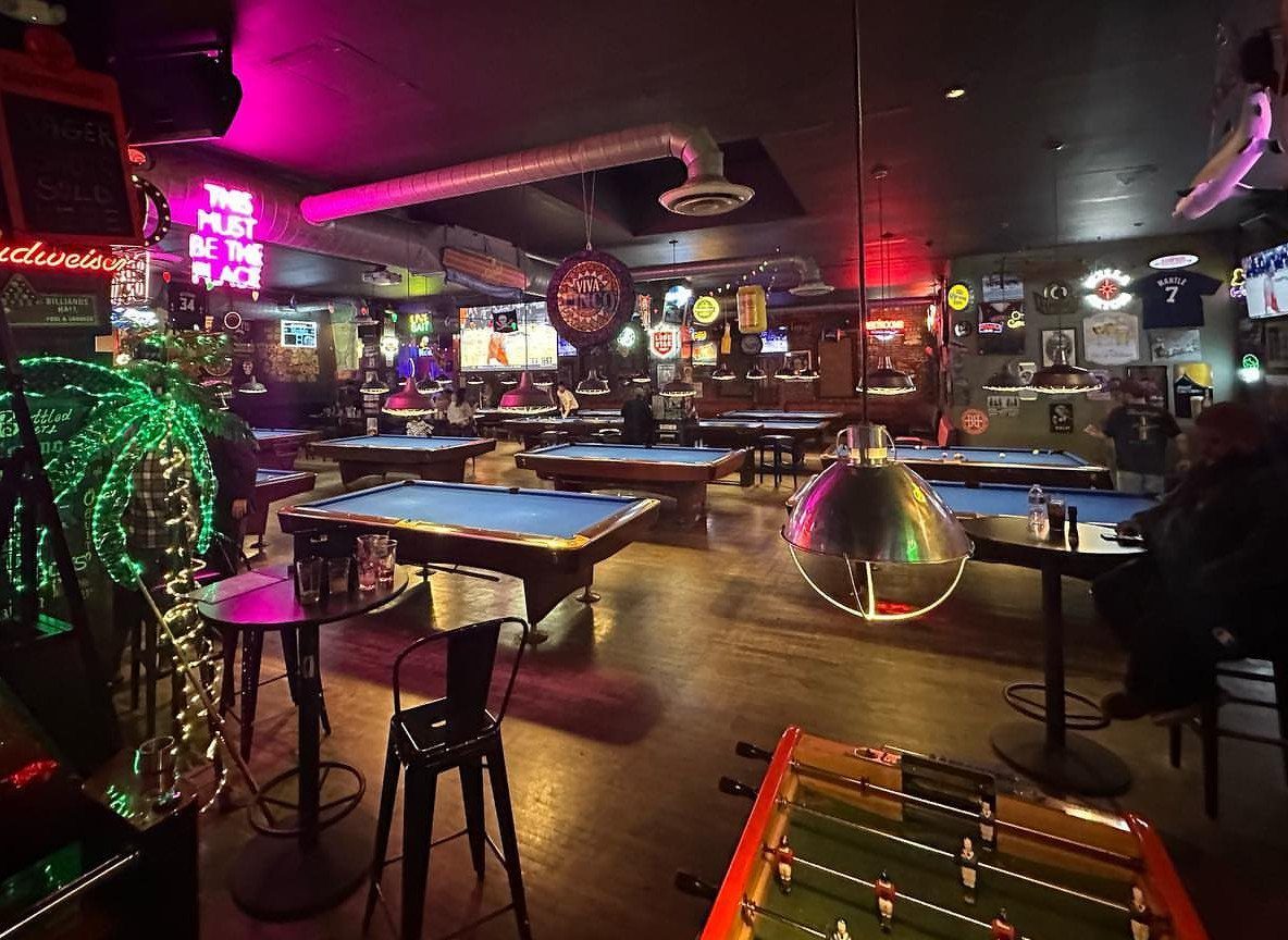 Multiple blue pool tables in a dimly lit bar with neon lighting.