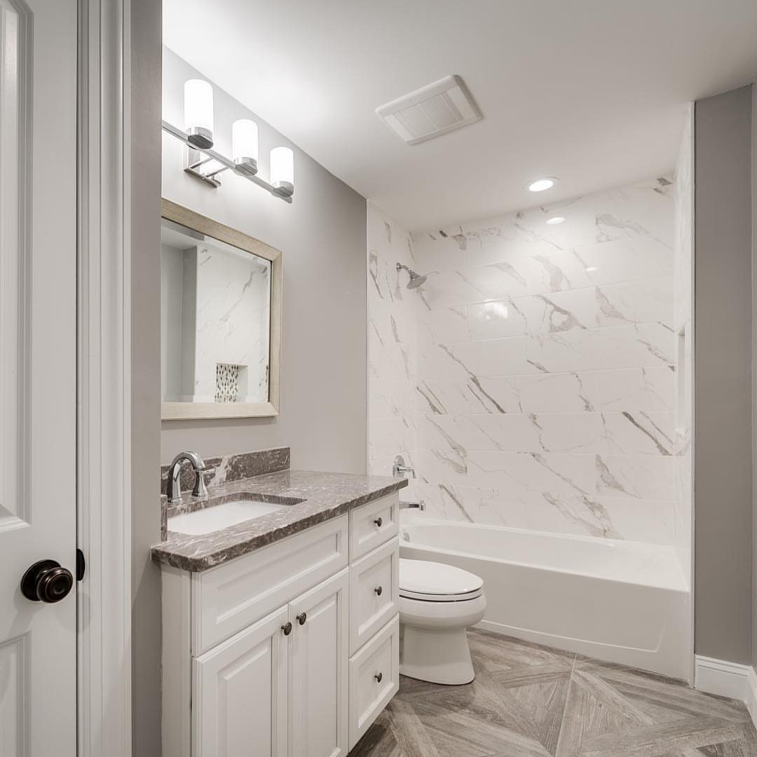 Modern bathroom with white vanity, marble tiles, and a white bathtub.