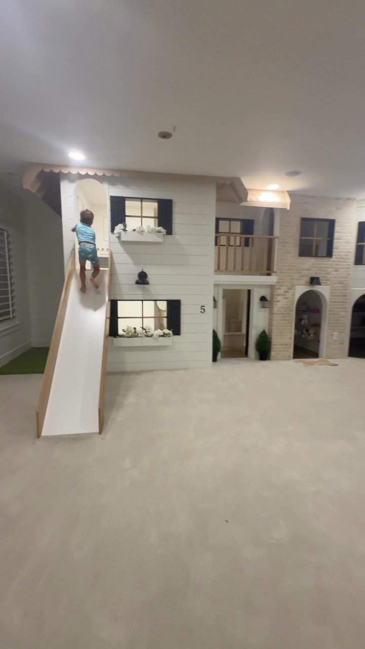 Child climbing a white slide attached to a custom indoor playhouse in a basement
