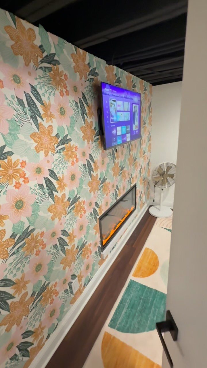 Floral wallpapered wall with a mounted television and linear fireplace in a basement.