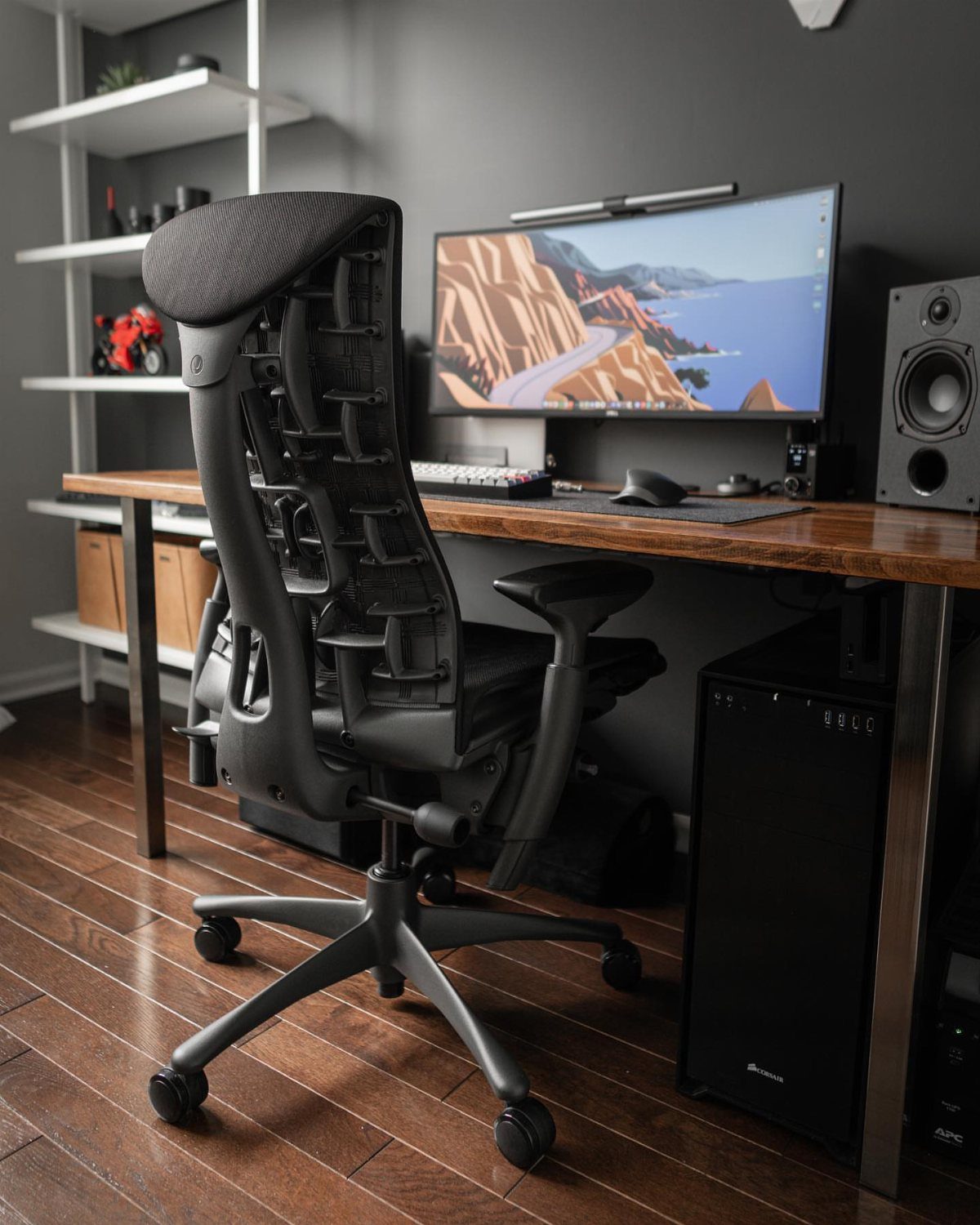 Ergonomic black mesh office chair and wooden desk with a wide computer monitor.