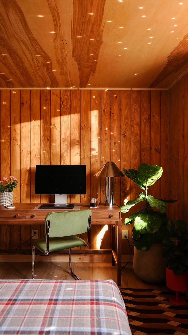 Wood-paneled home office with a green chair, computer desk, and large indoor plant.