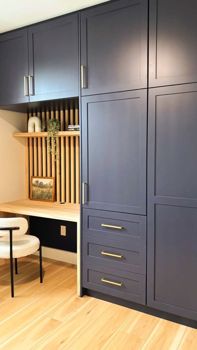 Home office nook with dark blue cabinets, wood slat wall, and light wood desk.