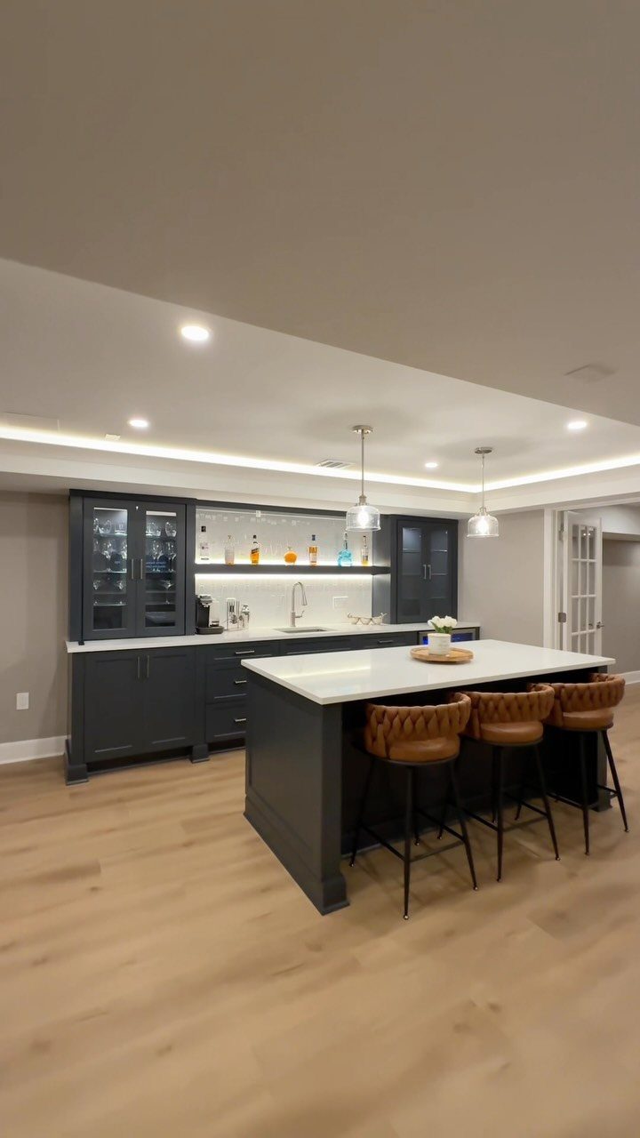 Modern basement bar with dark grey cabinets, white quartz island, and leather stools.