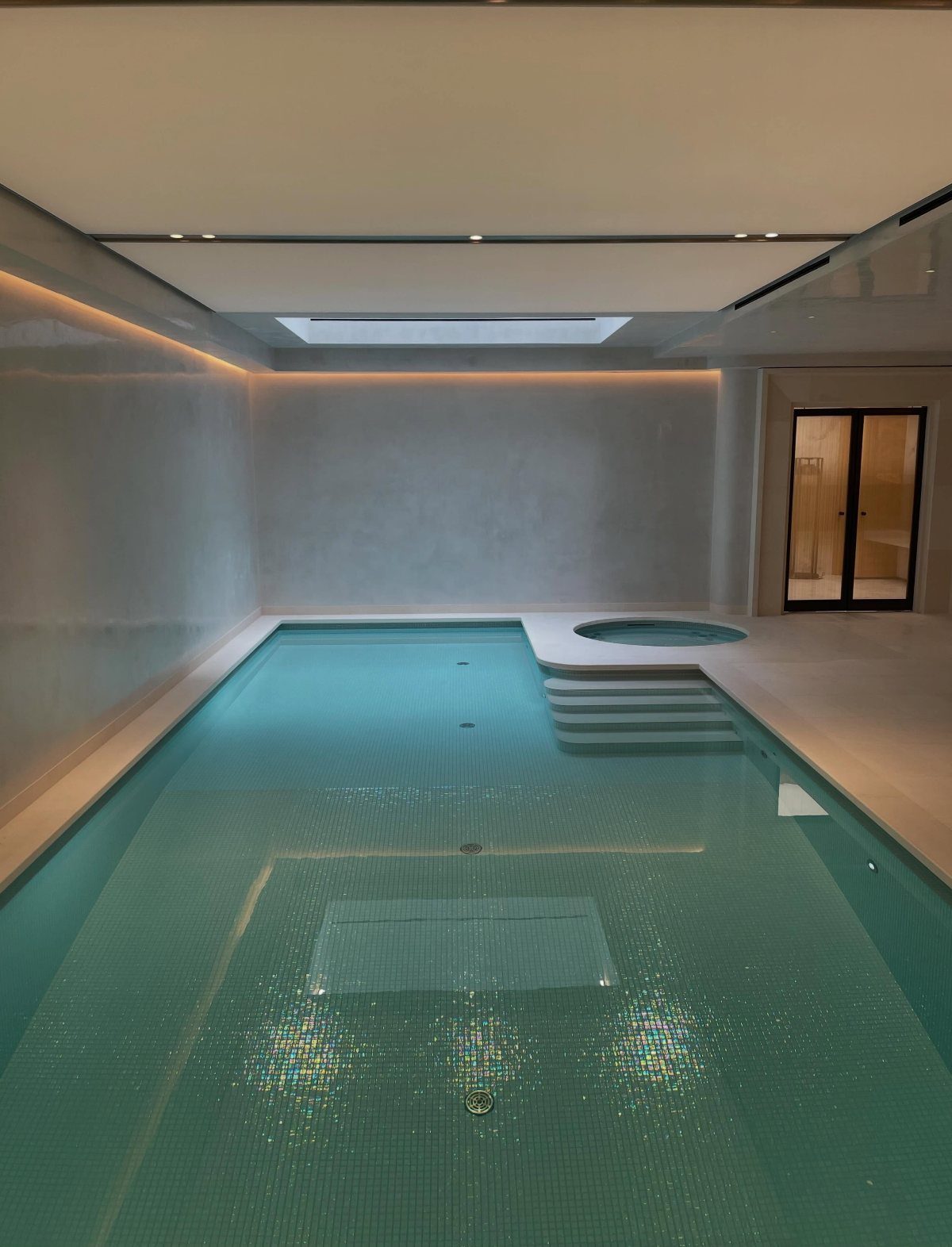 Indoor swimming pool with turquoise water and a small hot tub in a modern basement.