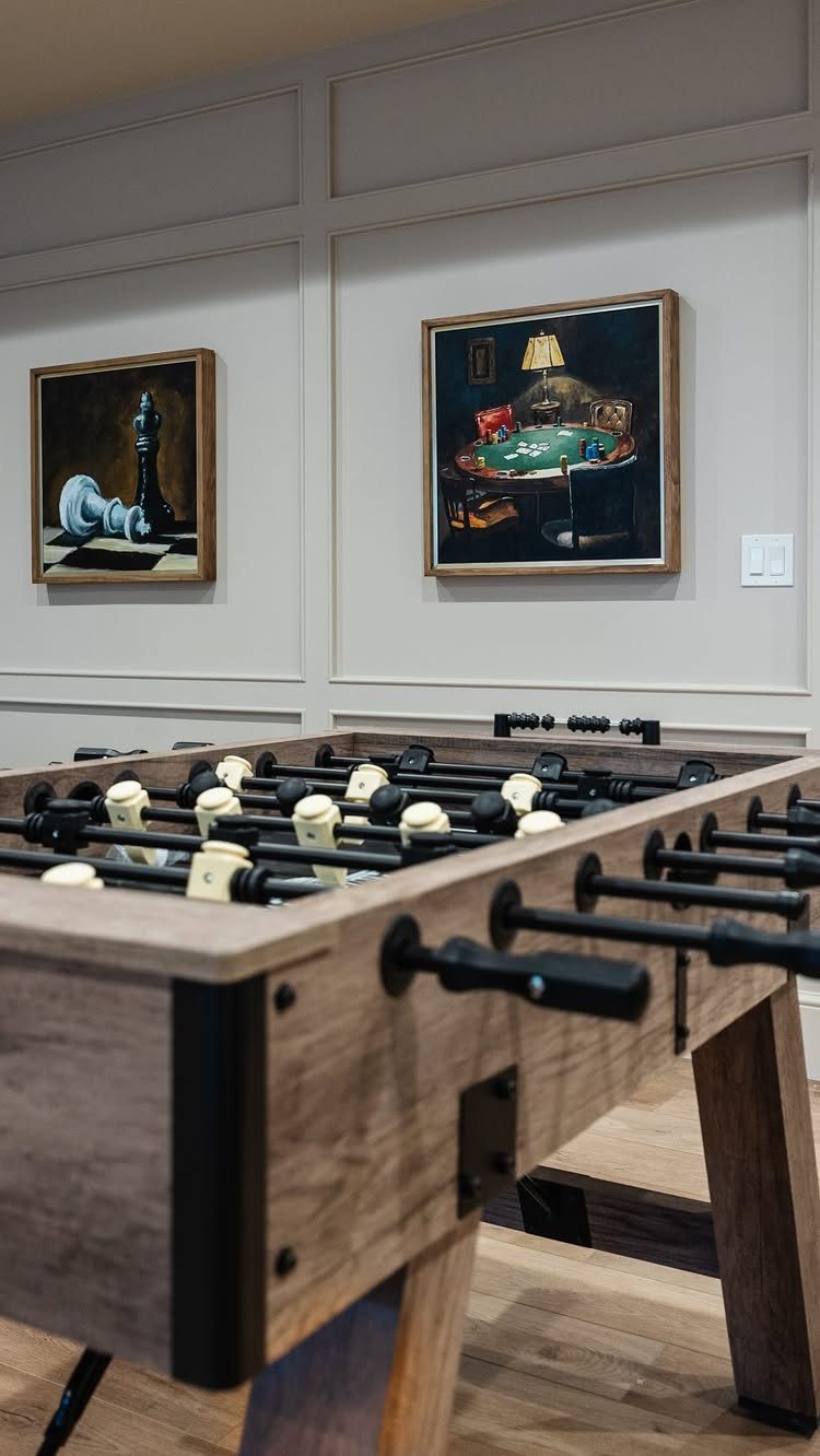 Wooden foosball table in a room with game-themed paintings on paneled walls.