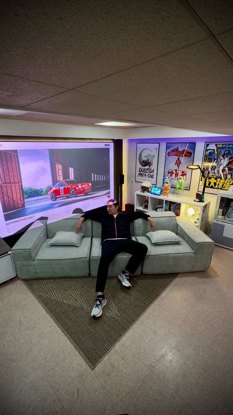 Person sitting on a grey sofa in front of a large home theater projector screen.