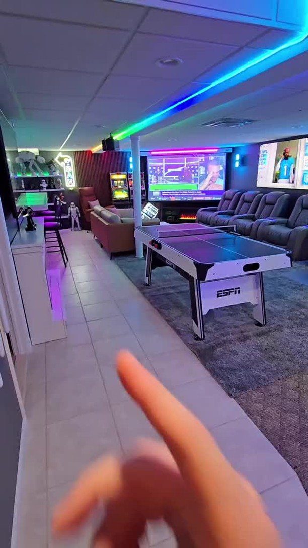 Basement game room with air hockey table, large screen, and neon LED lighting.