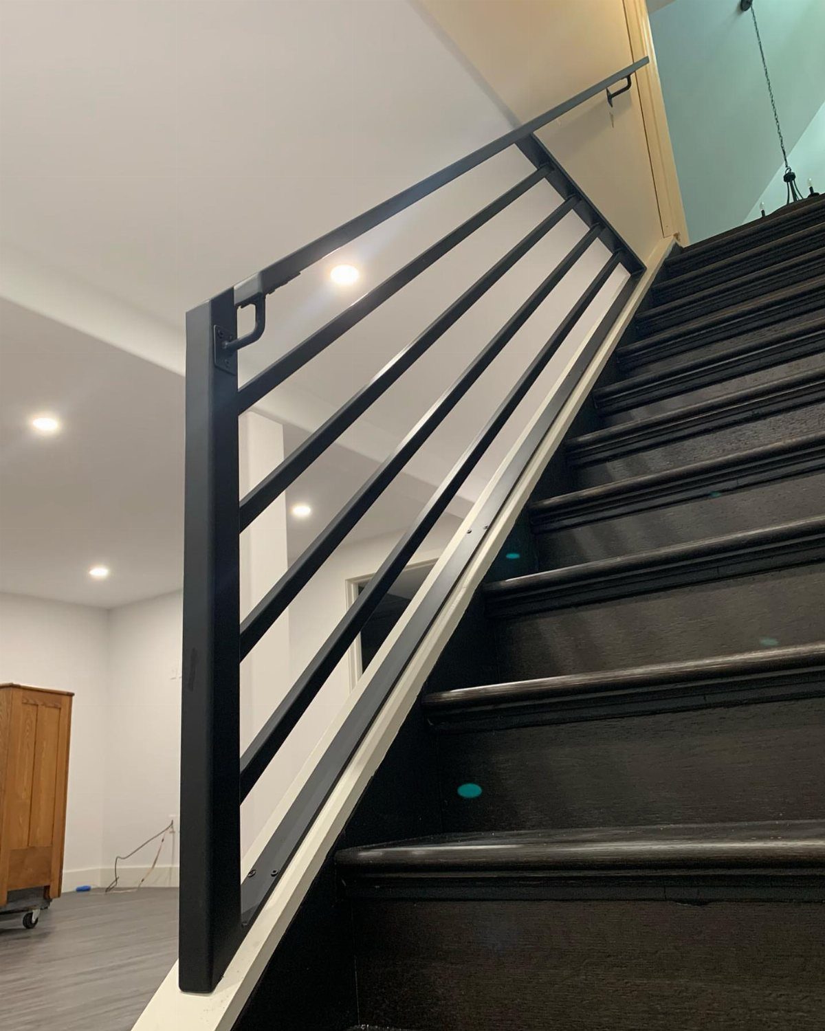 Modern black metal railing with horizontal balusters alongside dark wooden stairs.