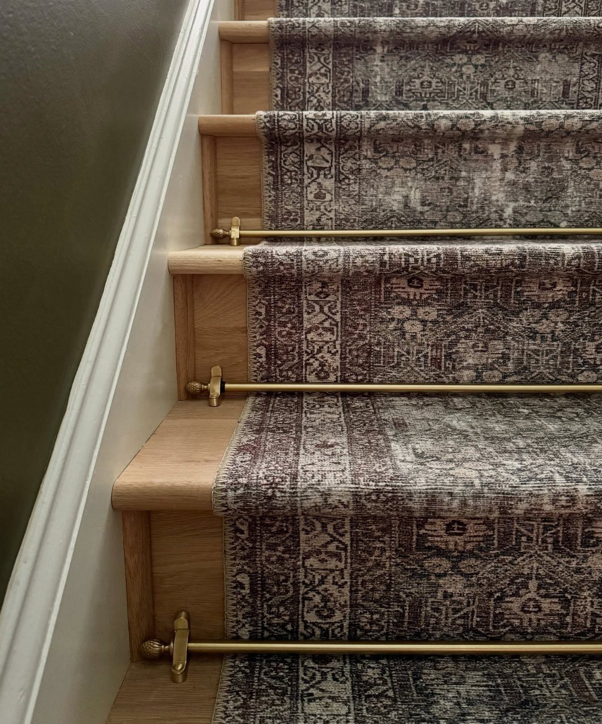 Patterned grey carpet runner on wooden stairs secured with gold metal stair rods.