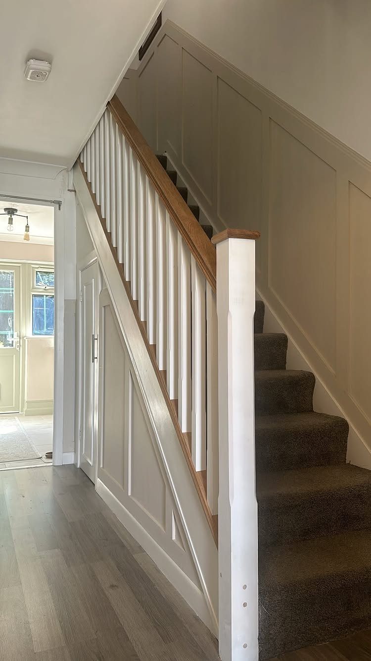Staircase with white vertical spindles, wooden handrail, and white board and batten walls.