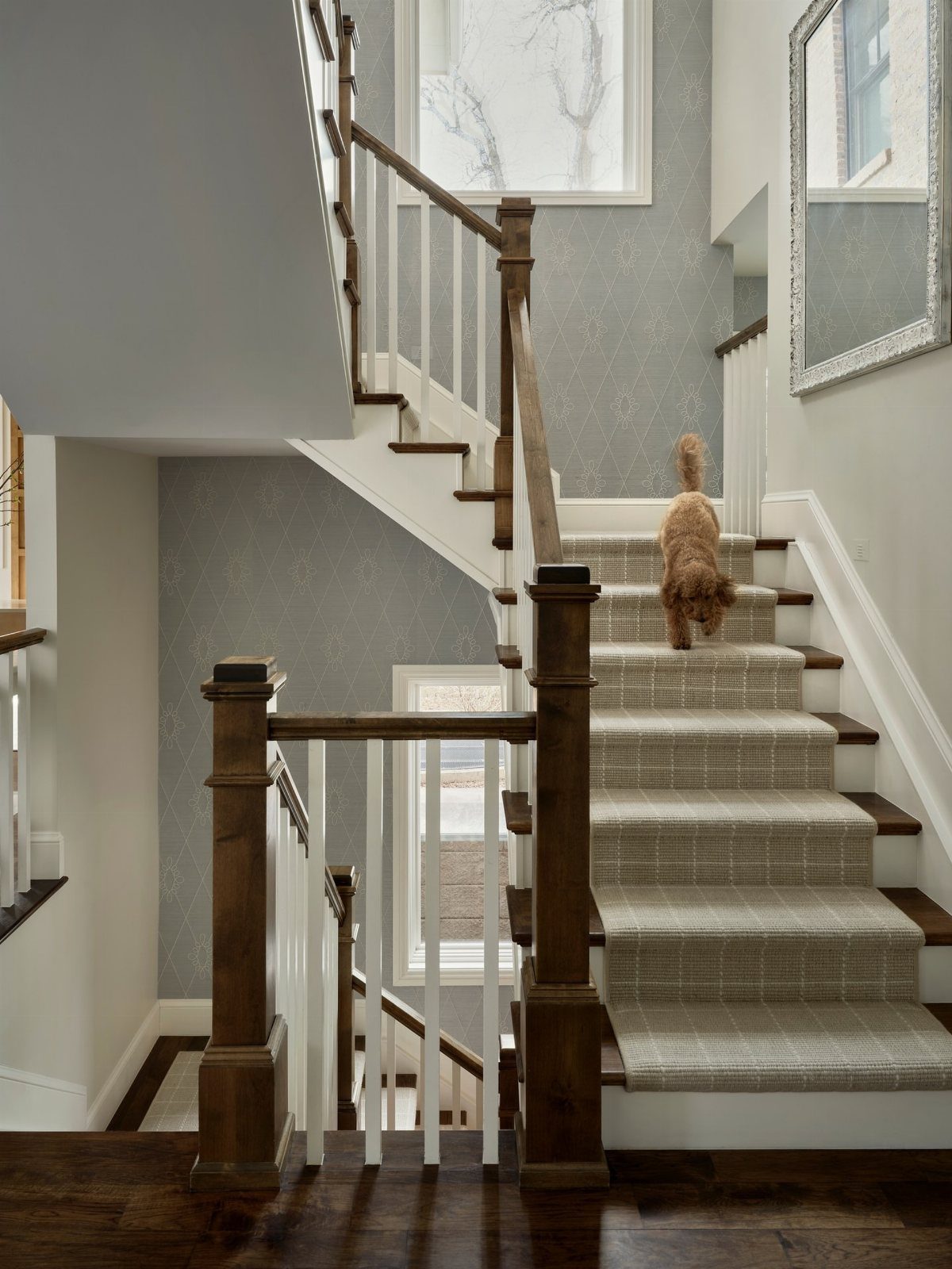 Staircase with light grey patterned wallpaper on the walls and a carpet runner.