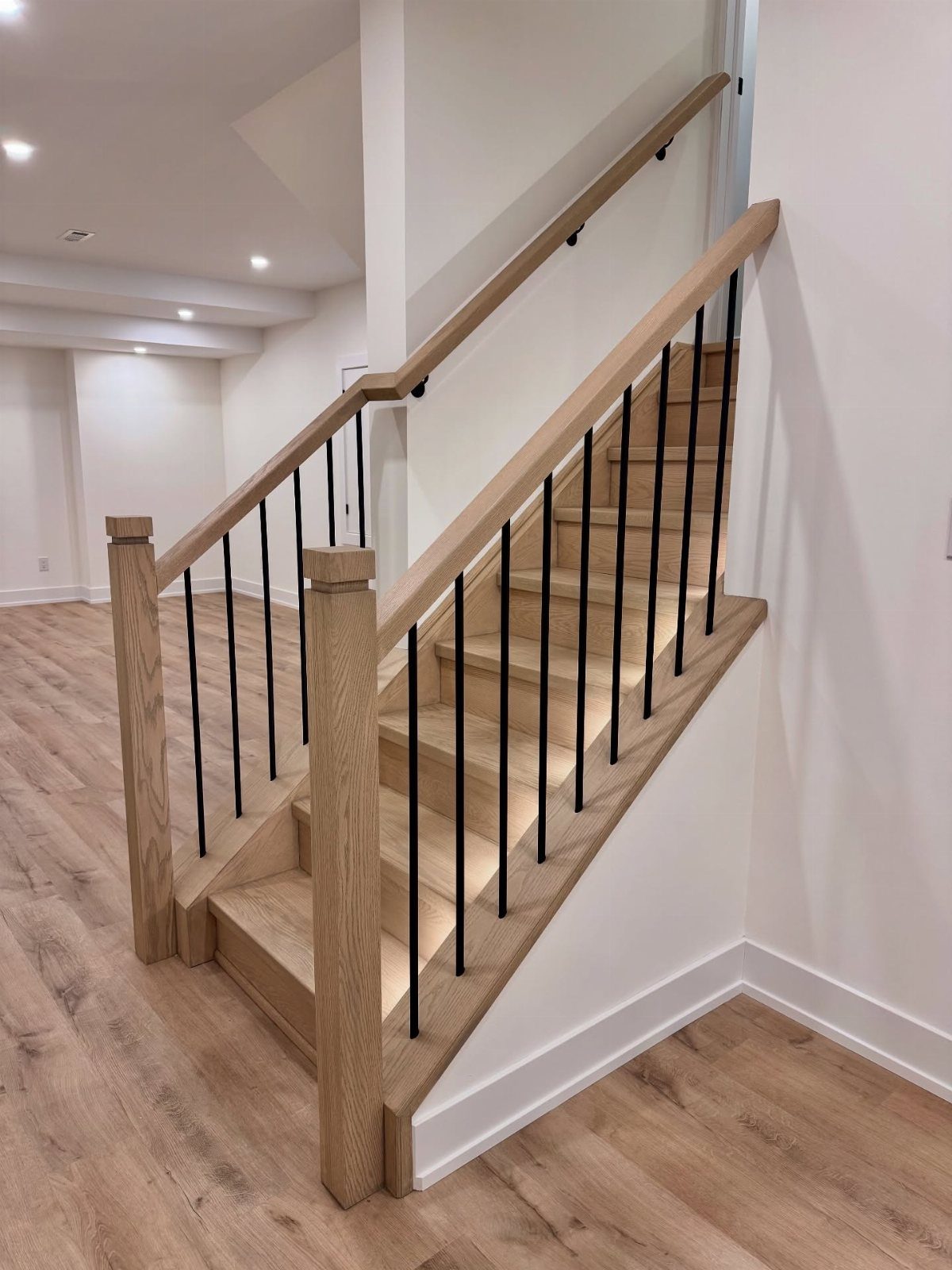 Light wood stairs with matching treads and risers and black metal spindles.