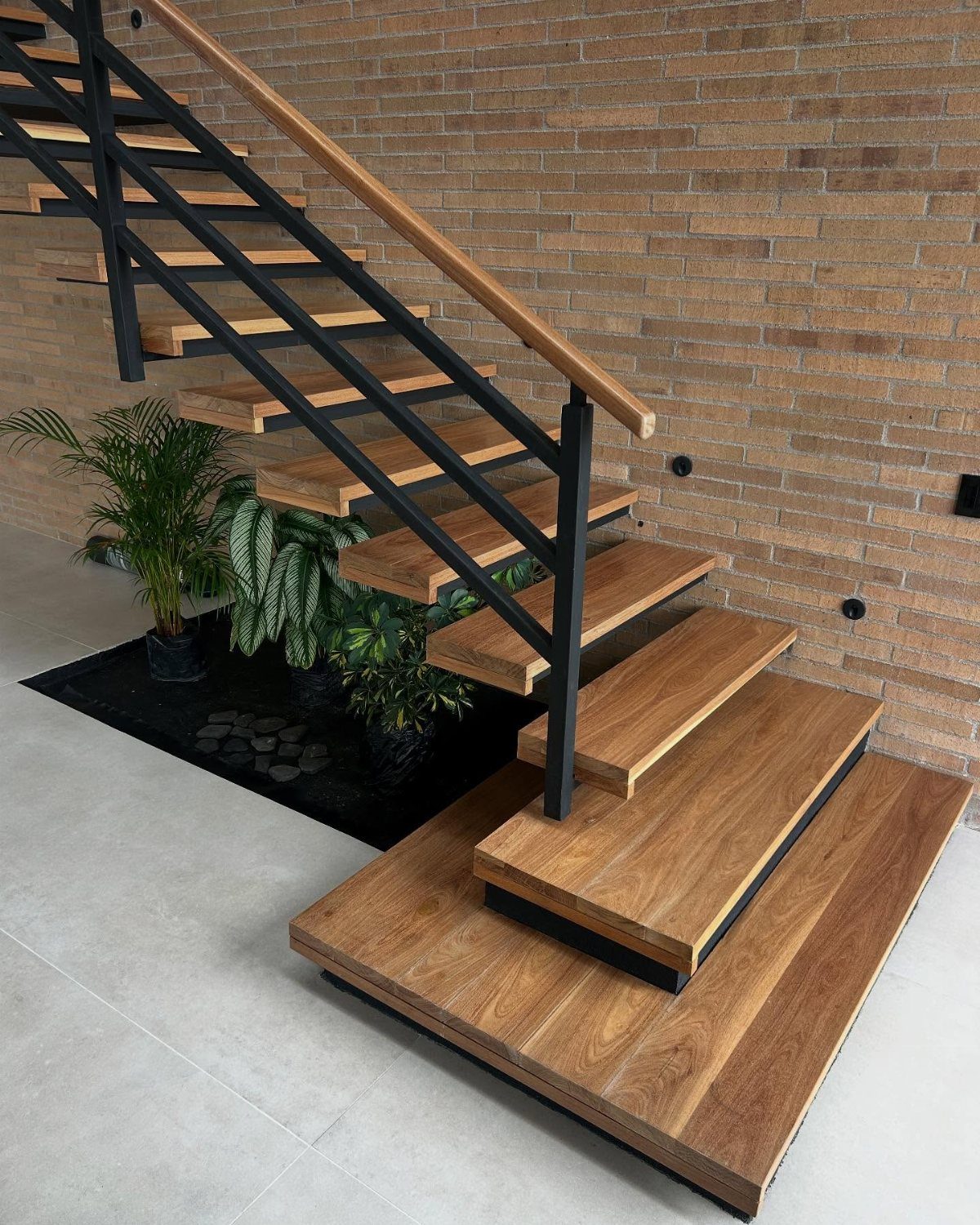 Wooden handrail on modern stairs with black metal railings and tan brick wall.