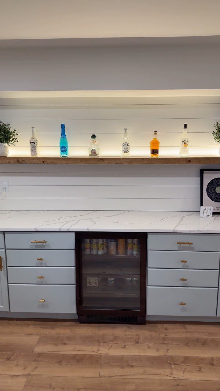 Farmhouse style home bar with white shiplap walls, marble counter, and rustic wooden shelf.