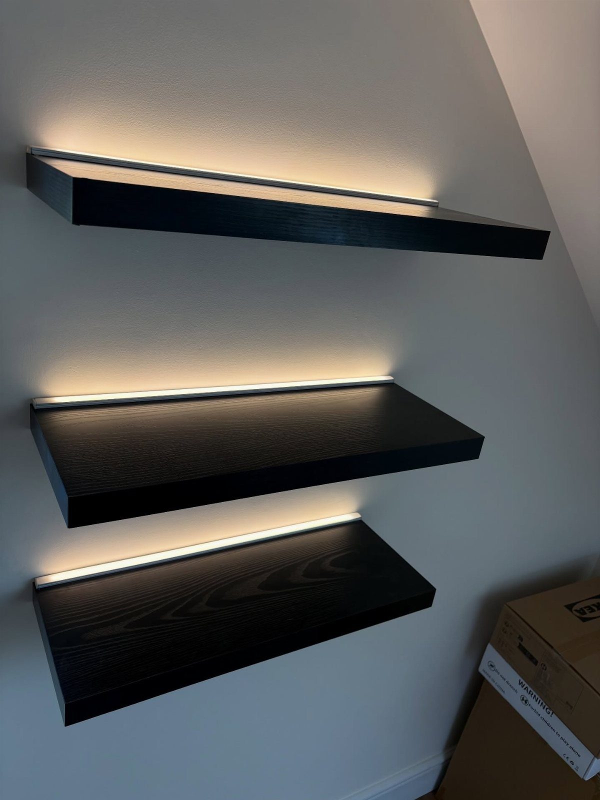 Black floating wooden shelves with integrated warm LED lighting on a grey wall