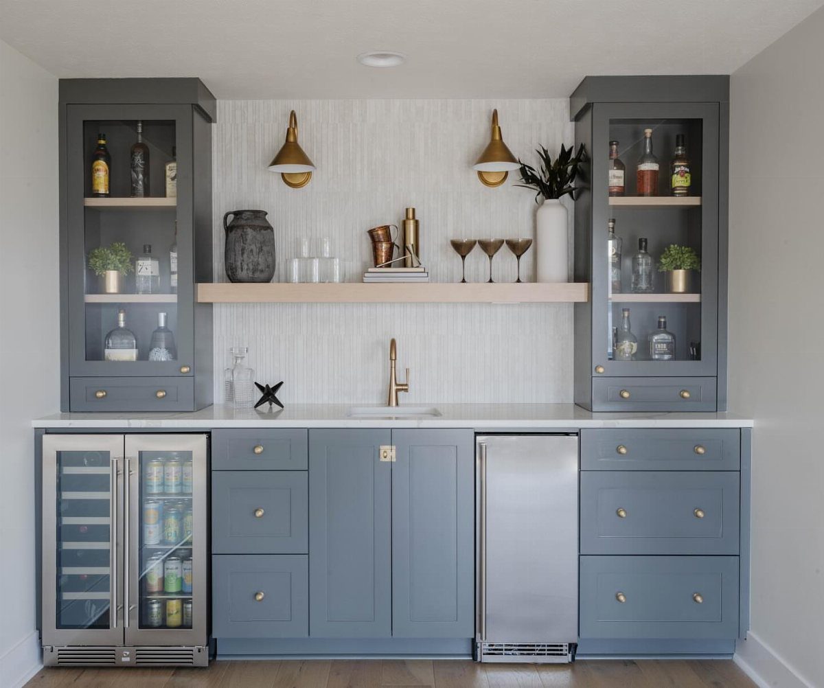 Grey home bar cabinetry with built-in stainless steel beverage coolers and gold wall sconces.