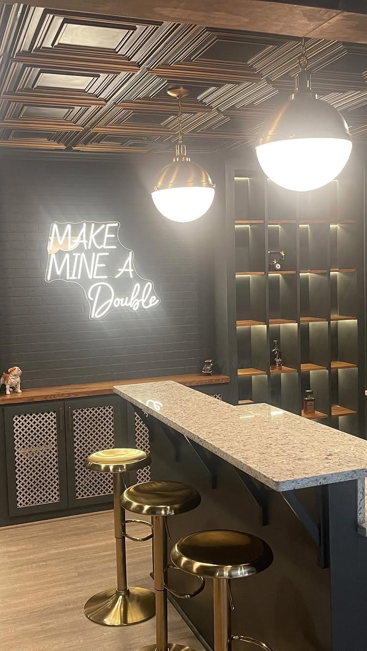 Two glowing dome pendant lights hanging over a modern home bar with gold stools.