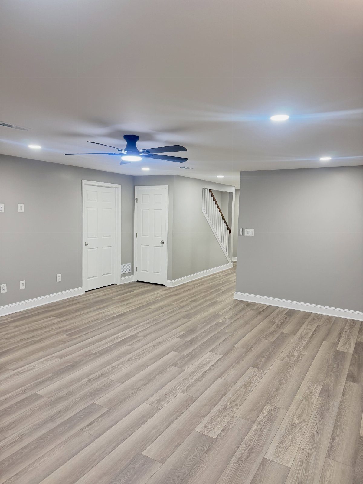10 Basement Wall Paint Ideas to Refresh Your Space 1 Light gray walls in an empty basement with wood-look flooring and white doors.