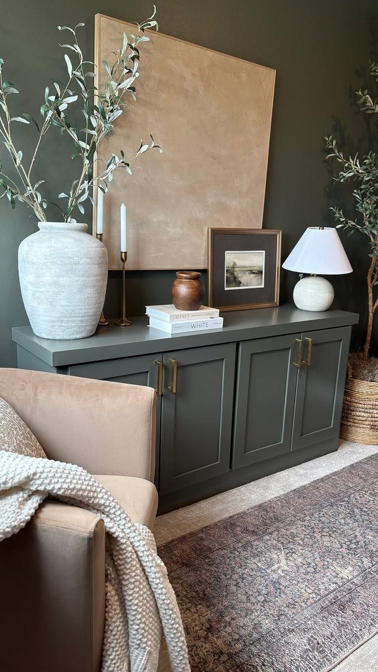 10 Basement Wall Paint Ideas to Refresh Your Space 6 Dark green wall with a gray sideboard and beige canvas leaning against it.