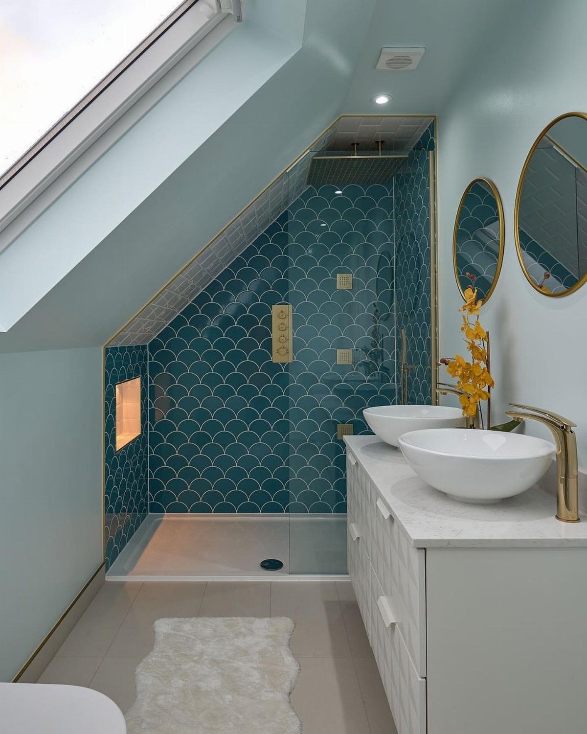 Attic bathroom with teal tiled shower, white double vanity, and a bright skylight.
