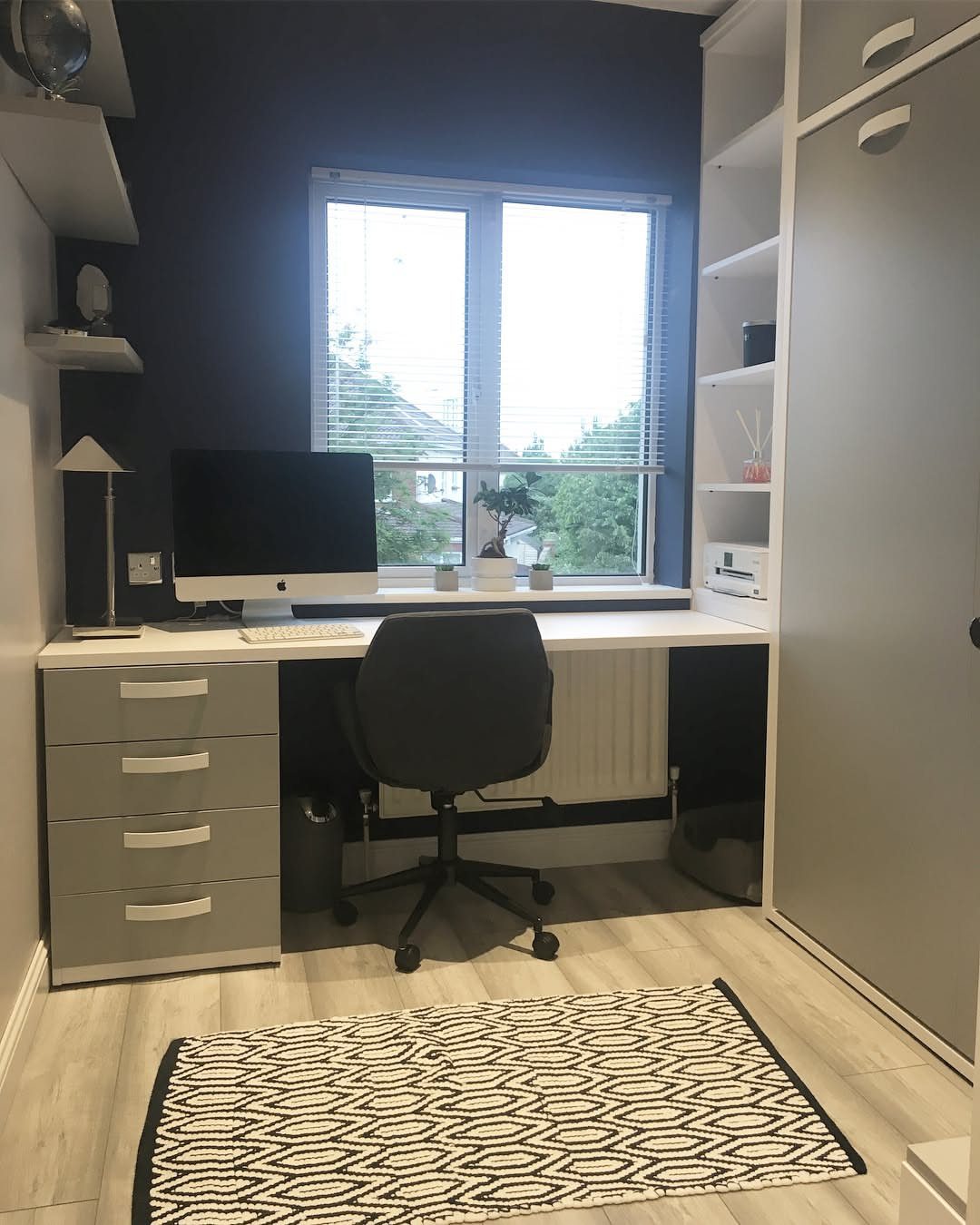 Home office workspace with a white desk, black chair, and dark blue wall.