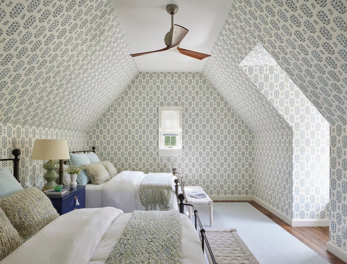 Attic bedroom with sloped patterned walls, twin beds, and a wooden ceiling fan.