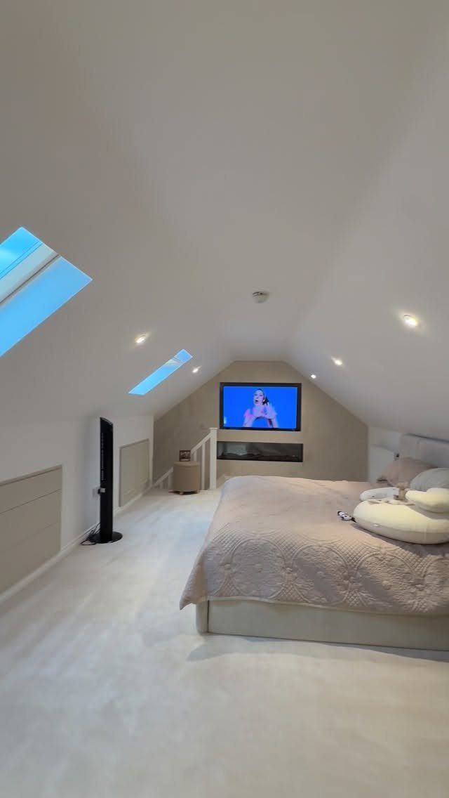 Modern attic bedroom with sloped ceilings, skylights, and a large bed with beige linens.