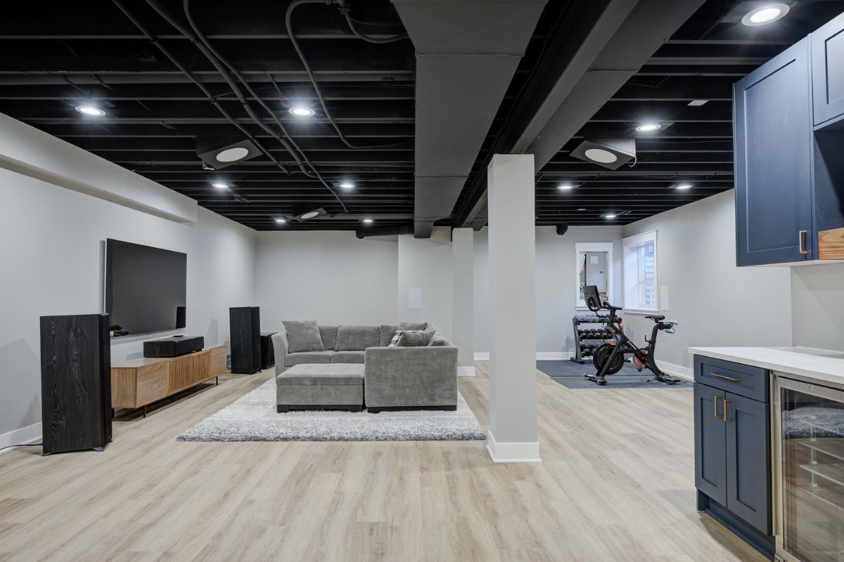11 Black Ceiling Basement Ideas with Real Impact 8 Finished basement with black painted open ceiling, grey sofa, and light wood floors.