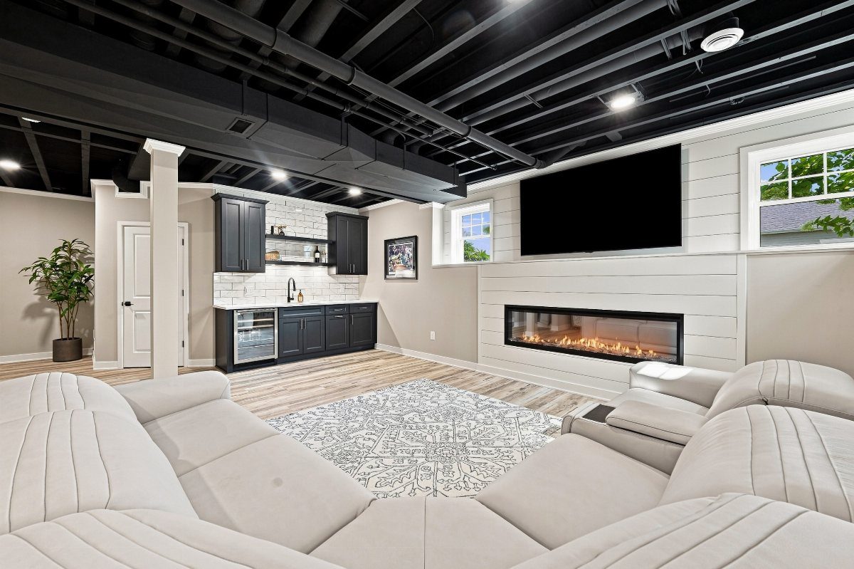 11 Black Ceiling Basement Ideas with Real Impact 4 Black painted ceiling beams in a modern basement with a white sectional and fireplace.