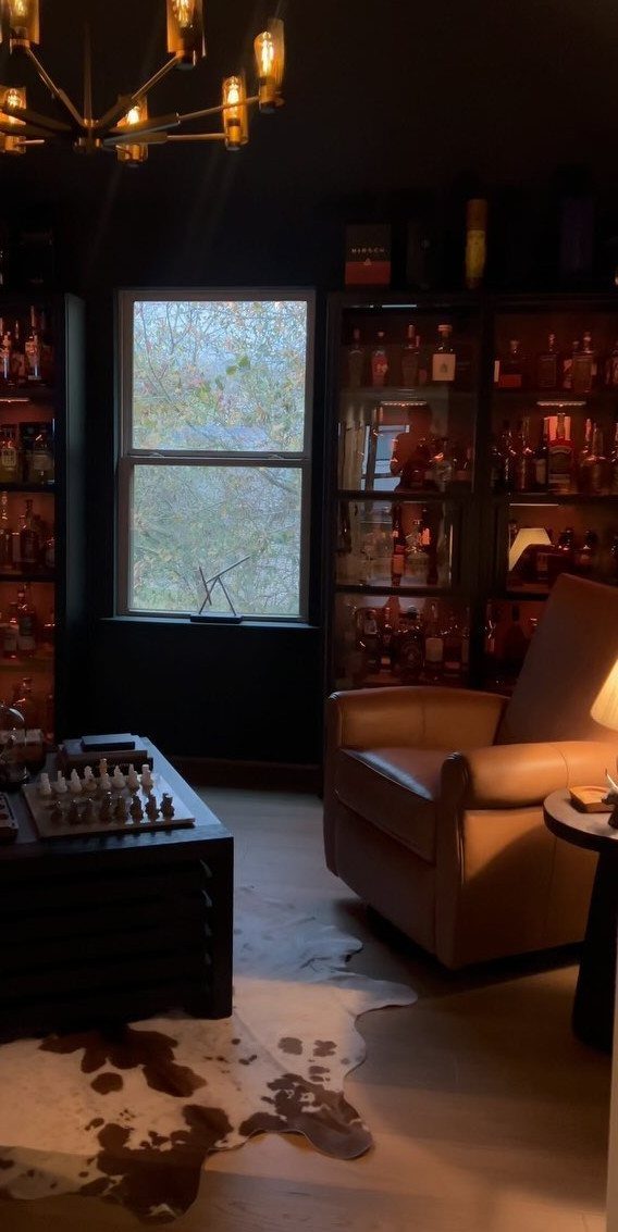 11 Black Ceiling Basement Ideas with Real Impact 7 Dark room with leather armchair, chess table, and gold chandelier under black ceiling.