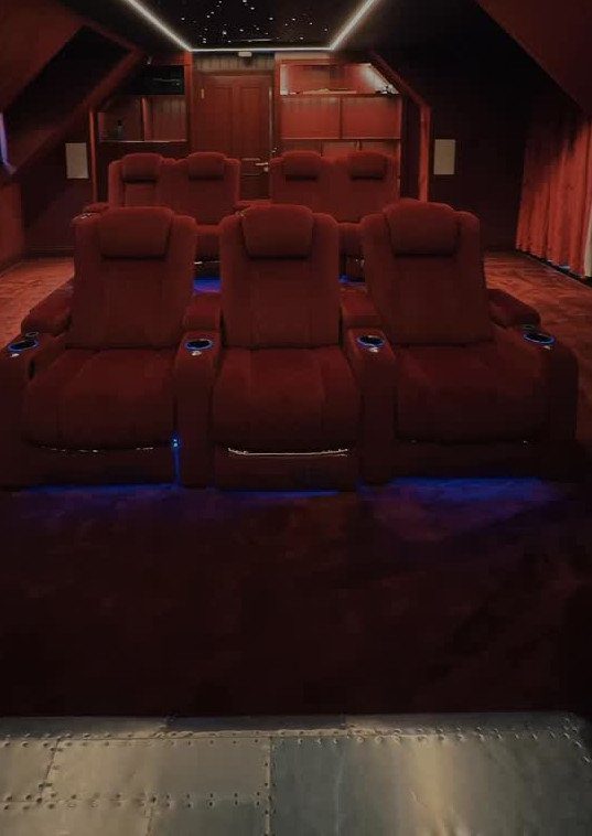 Red plush cinema seats on a dark red carpet in a home media room.