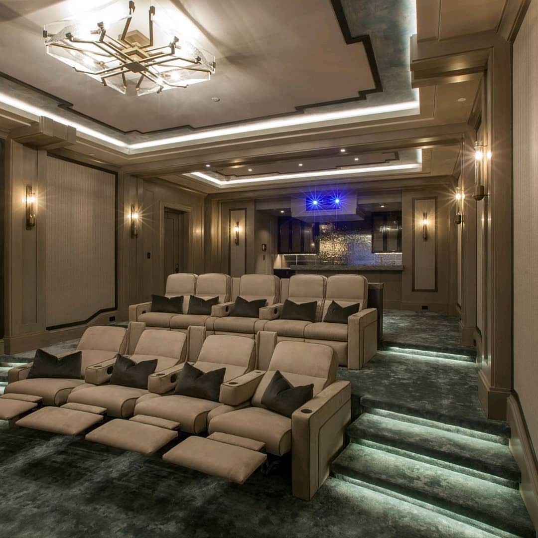 Luxury home cinema with tiered beige recliners and dark grey carpeting throughout.