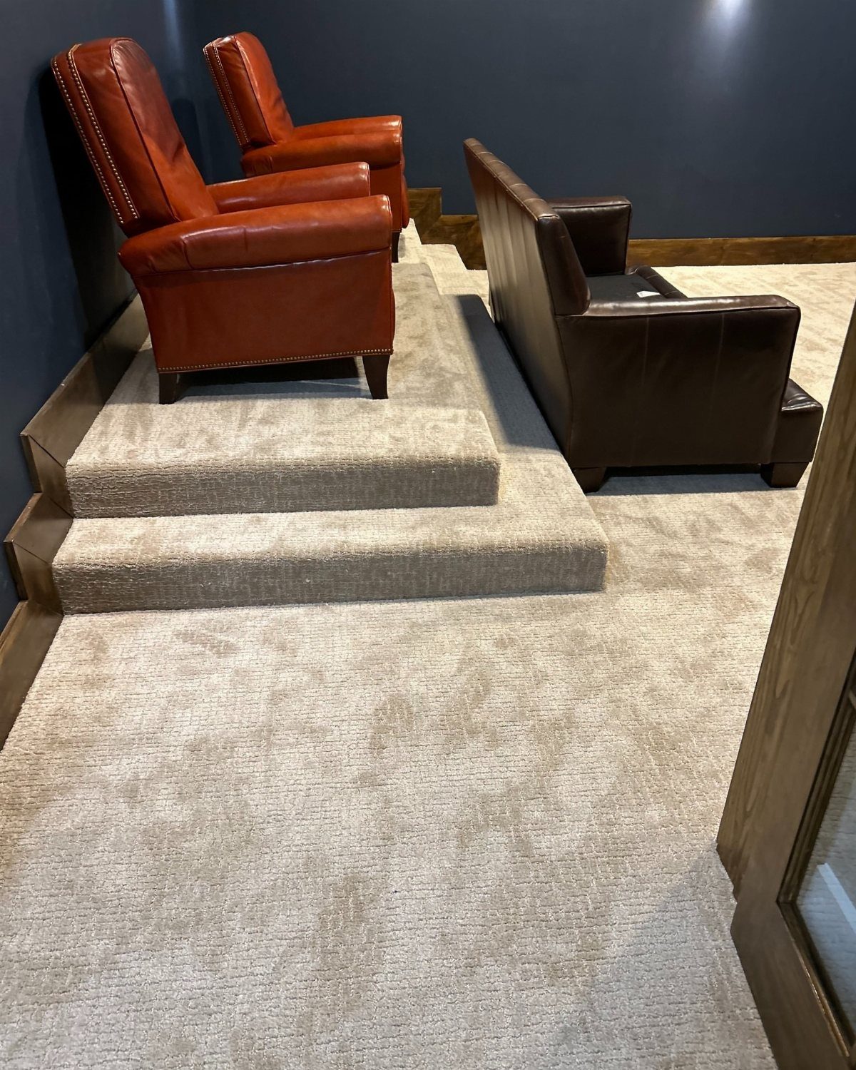 Beige wall-to-wall carpeting in a media room with tiered leather seating.