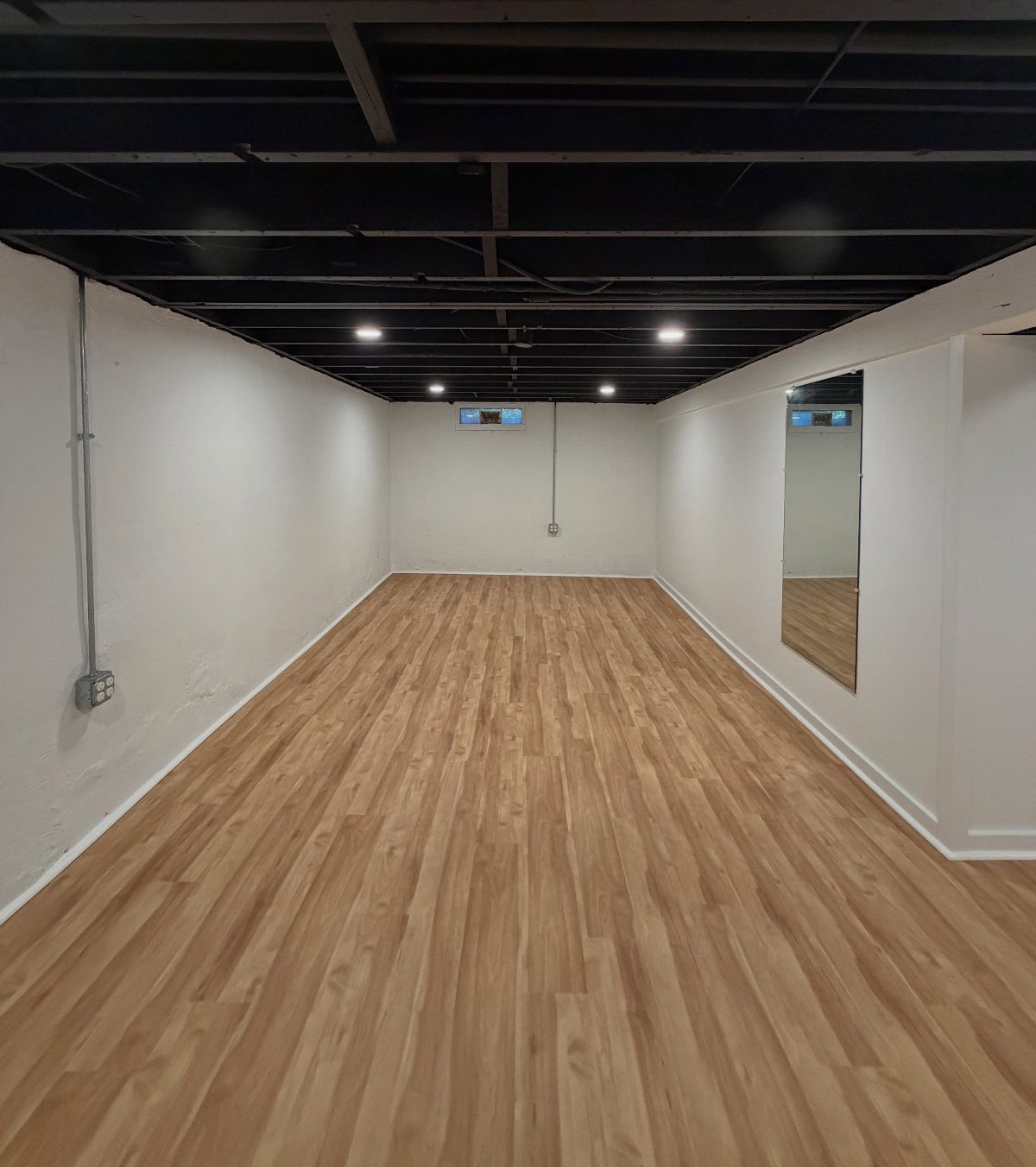 Black painted exposed ceiling in a room with light wood floors and white walls.