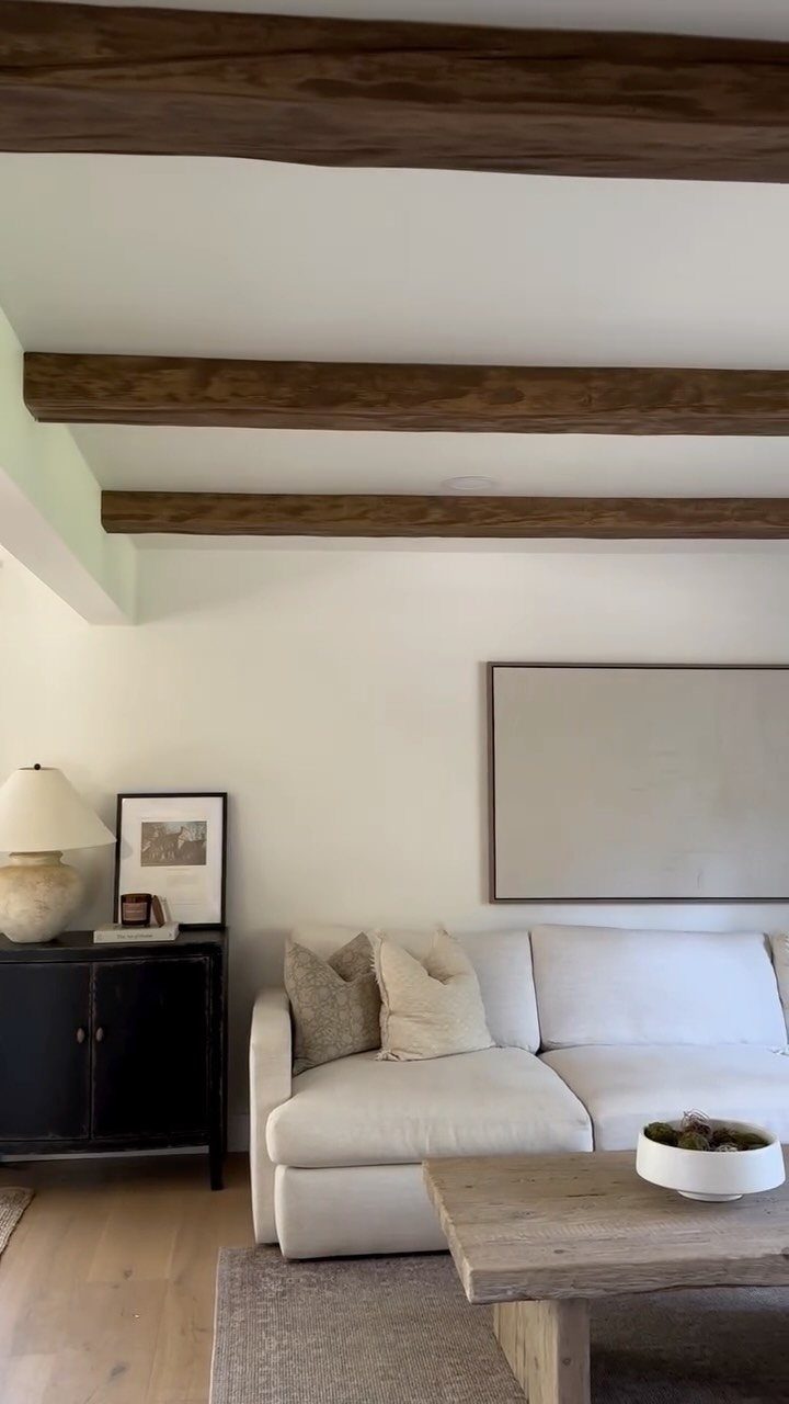 White ceiling with dark brown wooden beams above a white sofa and coffee table.