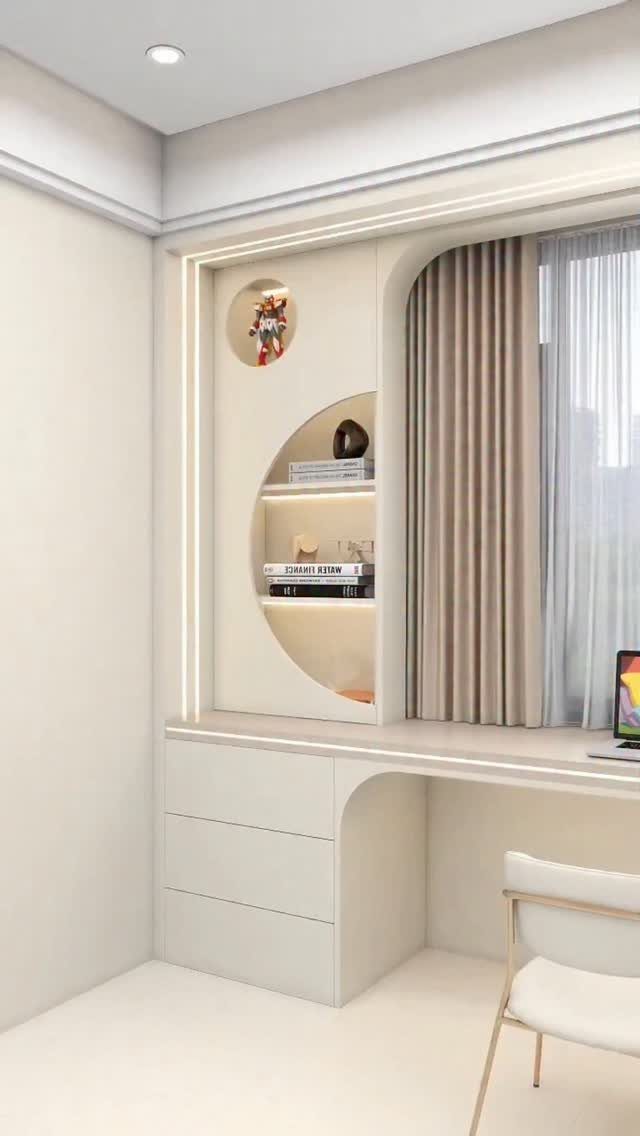 Built-in cream desk under a window with curved shelving and a white chair.