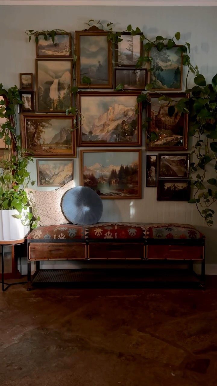 Gallery wall of framed landscape paintings with climbing green plants and a patterned bench.