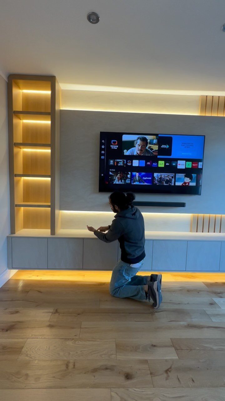 7 Family TV Room Ideas for a Comfortable Space 2 Wall-mounted television on a grey panel with warm lighting and floating white cabinets.